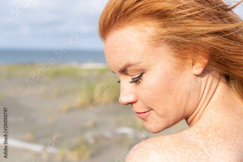 Beautiful woman with red hair and freckles at beach