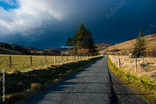 Dramatic dark sky with bright lit up landscape in the Perthshire part of the Scottish Highlands. Photograph taken in November on a sunny day in Scotland.