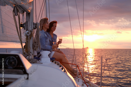 Pair of best friend are taking boat trip on the yacht at suset time with few glasses of wine. © Fxquadro
