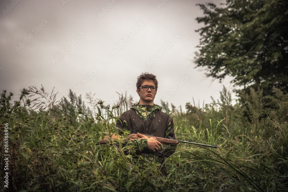 Hunting hunter boy with gun hiding in tall grass during hunting season