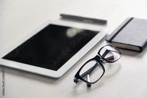 lentes, tableta, libreta y lapicera sobre fondo blanco