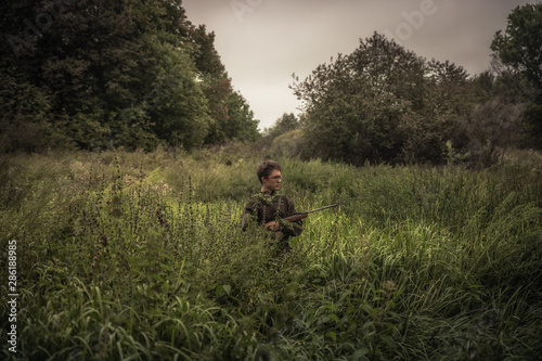 Hunting hunter boy with gun hiding in tall grass during hunting season