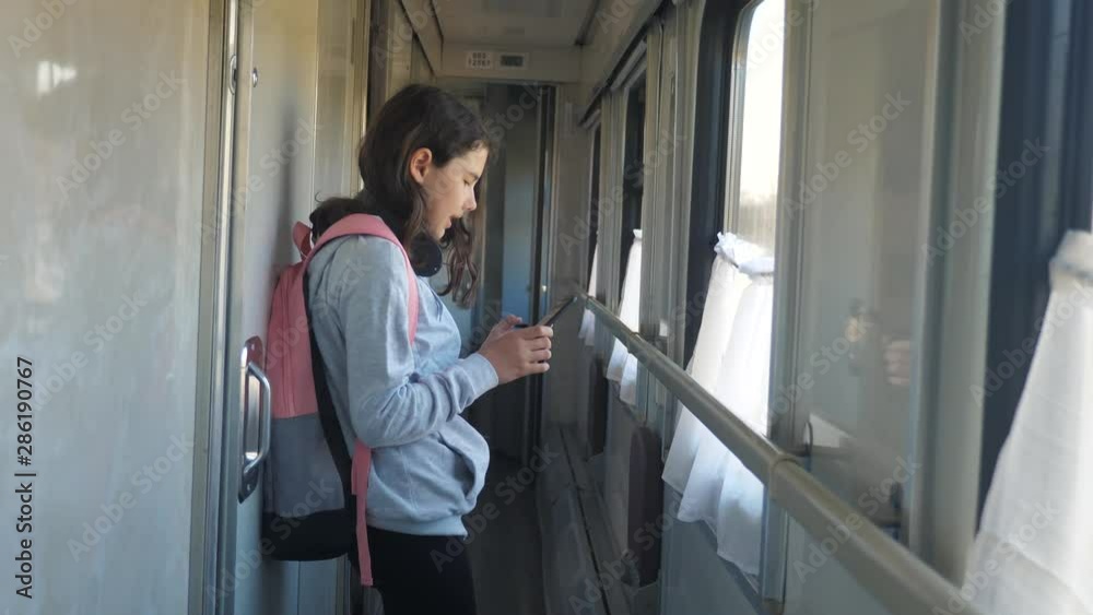 little girl walks on a train compartment car with a backpack lifestyle and a smartphone. travel transportation railroad concept. the girl in the train at the window corresponds the girl in the train little girl walks on a train compartment car with a backpack lifestyle and a smartphone. travel transportation railroad concept. the girl in the train at the window corresponds the girl in the train