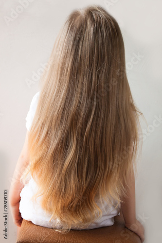 Cute girl with long blond hair. Back view of little girlie looking on side. Isolated on light background.