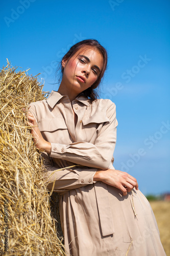 Beautiful girl in a beige dress posing on a background of haystacks in a cut field