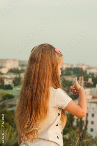 Little girl with long blond hair in a white T-shirt on a nature background.