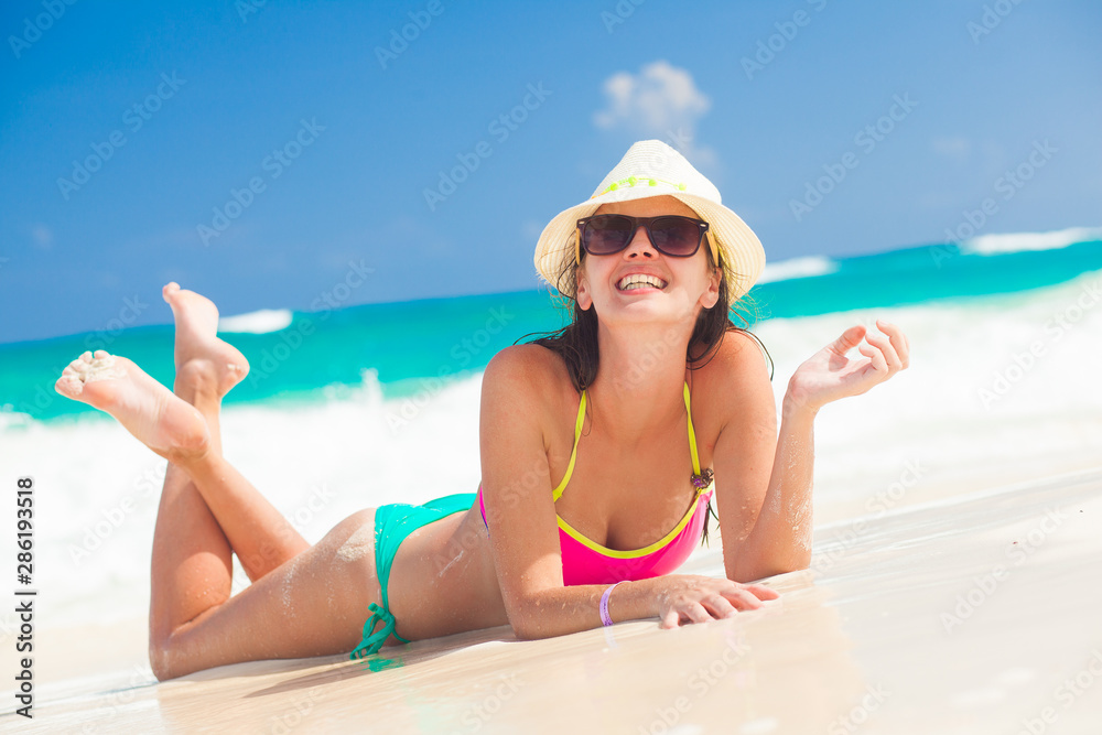 Young woman in bikini and straw hat relaxing at white caribbean beach