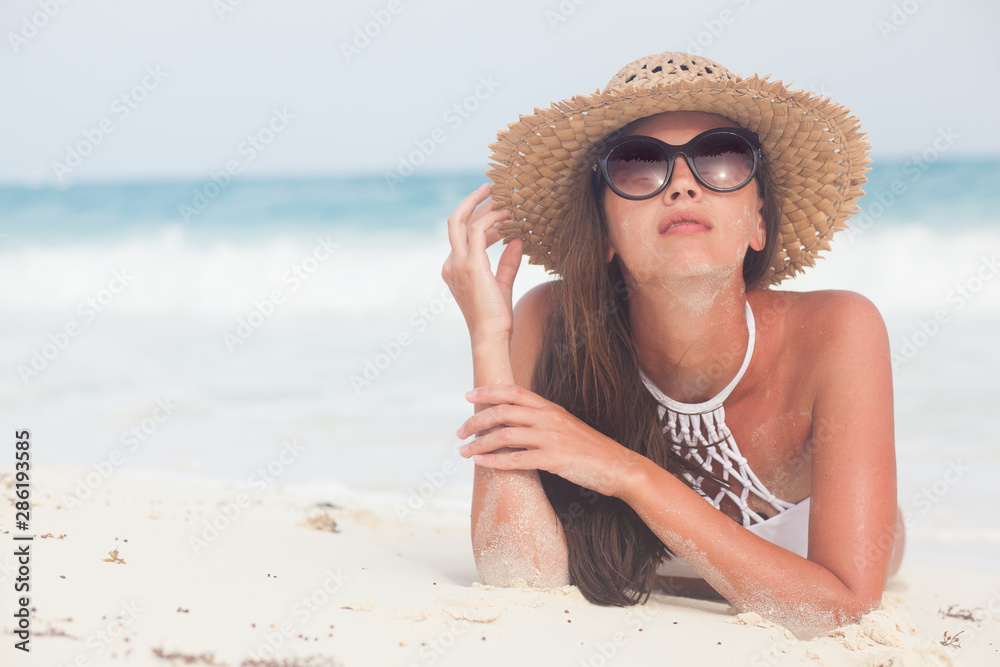 Young woman in bikini and straw hat relaxing at white caribbean beach