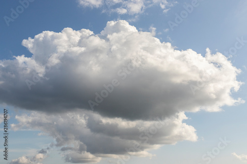 Blue sky with white clouds. Big dark cloud on the blue sky. Cloudy daytime weather. Background with free space and empty place.