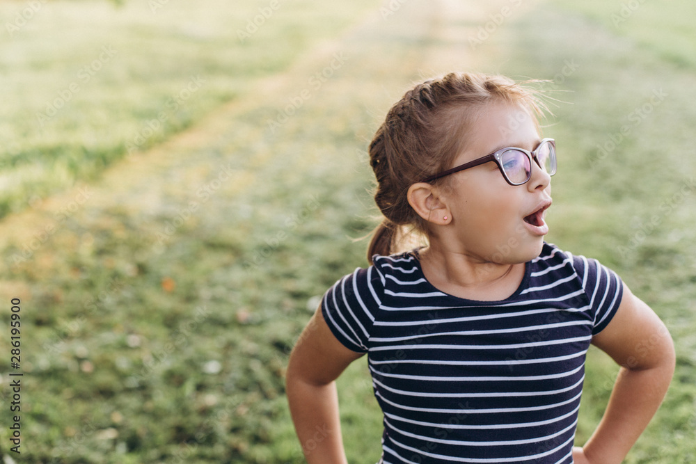 Cheerful emotional portrait of little girl with poor eyesight in eyeglasses outdoors in summer park Cheerful emotional portrait of little girl with poor eyesight in eyeglasses outdoors in summer park