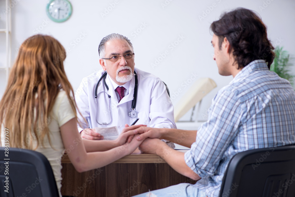 Fototapeta premium Young couple visiting old male doctor