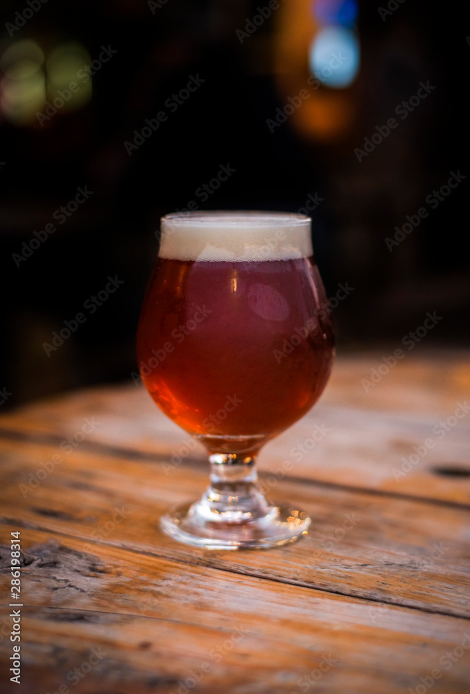 amber beer in tulip glass, craft beer on the patio, patio table with beer, patio lights, microbrewery, people in the background amber beer in tulip glass, craft beer on the patio, patio table with beer, patio lights, microbrewery, people in the background