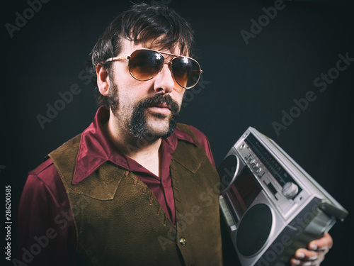 Man wearing authentic 1970's or early 1980's era clothing and sunglasses, holding a vintage silver portable cassette boombox. photo