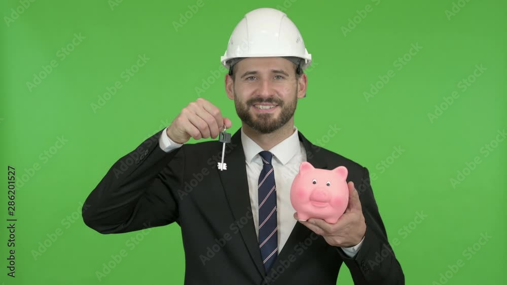 Happy Engineer holding Piggy Bank with House key against Chroma Key Happy Engineer holding Piggy Bank with House key against Chroma Key