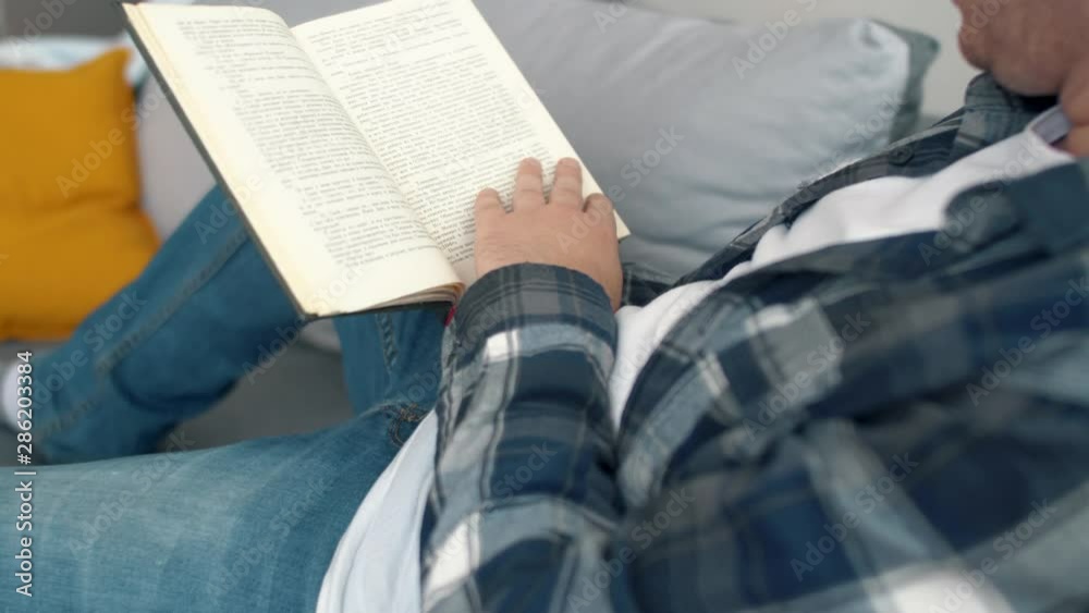 Man seat on sofa in living room and read book. Relaxing after work. Lifestyle. 4k slow motion footage. Man seat on sofa in living room and read book. Relaxing after work. Lifestyle. 4k slow motion footage.