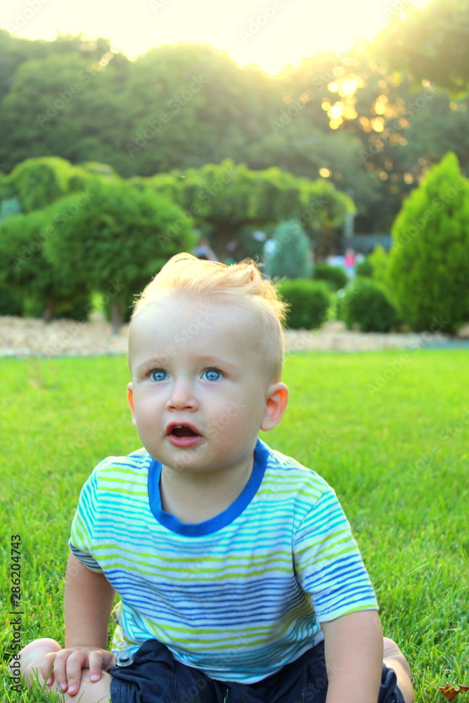 Little blond boy plays with a multi-colored ball on the grass in the park, selective focus. Little blond boy plays with a multi-colored ball on the grass in the park, selective focus.