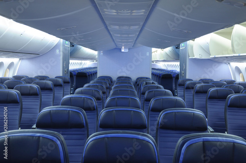 Empty commercial airplane cabin interior with blue leather seats. Two aisles and open overhead bins