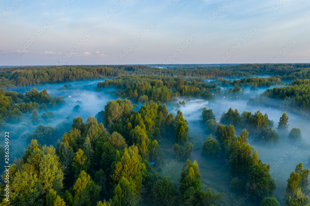 Aerial view of the forest, field and river covered with layers of thick morning fog