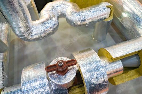 Pipes with a layer of insulating material and foil. Pipes with brown valve. Foil insulation for pipes. Demonstration of thermal insulation properties of insulation with foil.