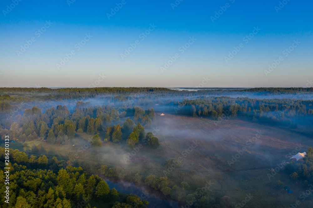 Fog floats over the forest and a field and a star-shaped tent