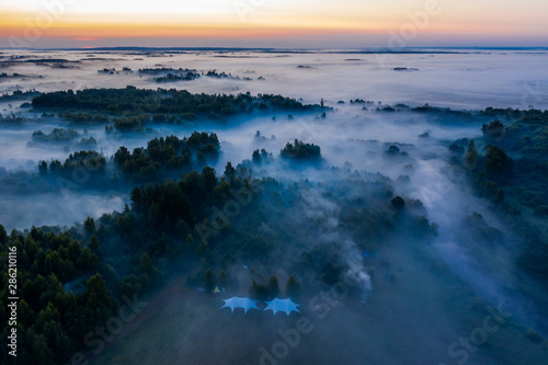 Fog floats over the forest and a field and a star-shaped tent