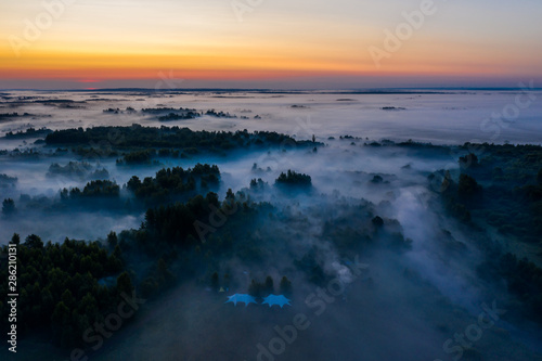 Fog floats over the forest and a field and a star-shaped tent © alexkazachok