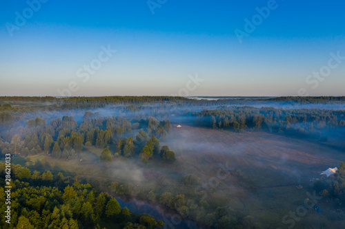 Fog floats over the forest and a field and a star-shaped tent