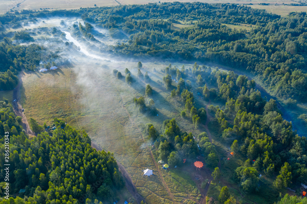 Fog floats over the forest and a field and a star-shaped tent