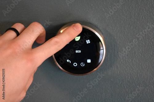 Hand operating smart thermostat to save money