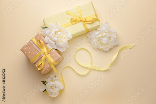 Gift boxes and beautiful flowers on color background