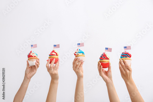 Female hands with tasty patriotic cupcakes on white background