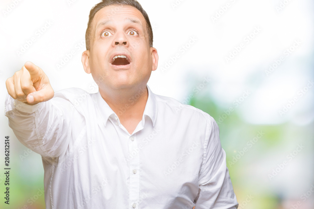 Middle age arab elegant man over isolated background Pointing with finger surprised ahead, open mouth amazed expression, something in front Middle age arab elegant man over isolated background Pointing with finger surprised ahead, open mouth amazed expression, something in front