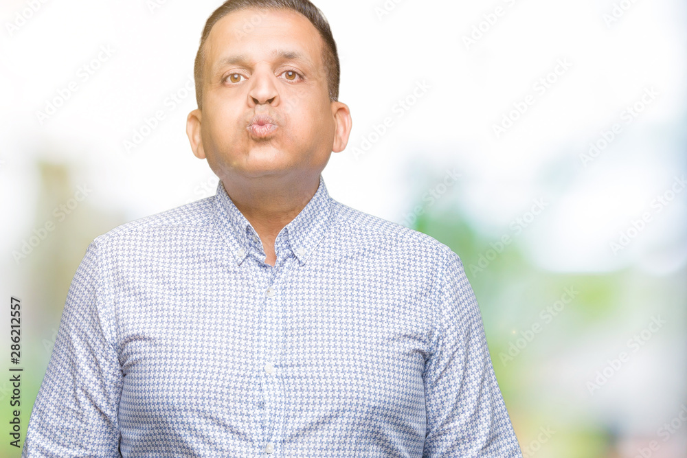 Middle age arab business man over isolated background puffing cheeks with funny face. Mouth inflated with air, crazy expression.
