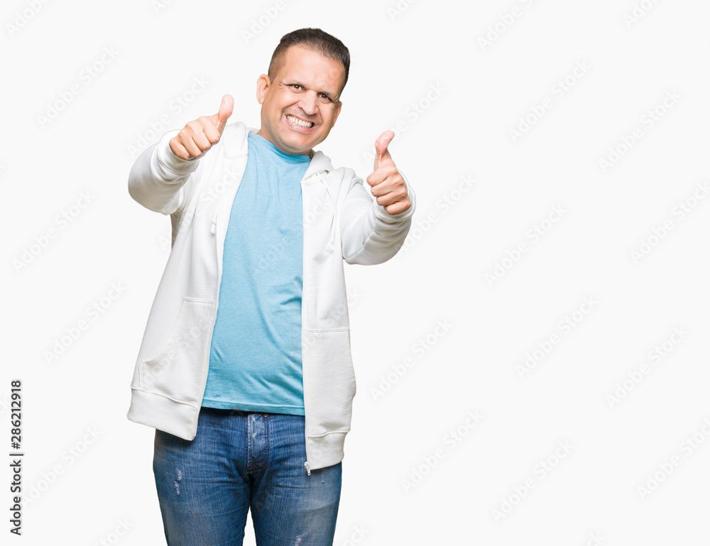 Middle age arab man wearing sweatshirt over isolated background approving doing positive gesture with hand, thumbs up smiling and happy for success. Looking at the camera, winner gesture.