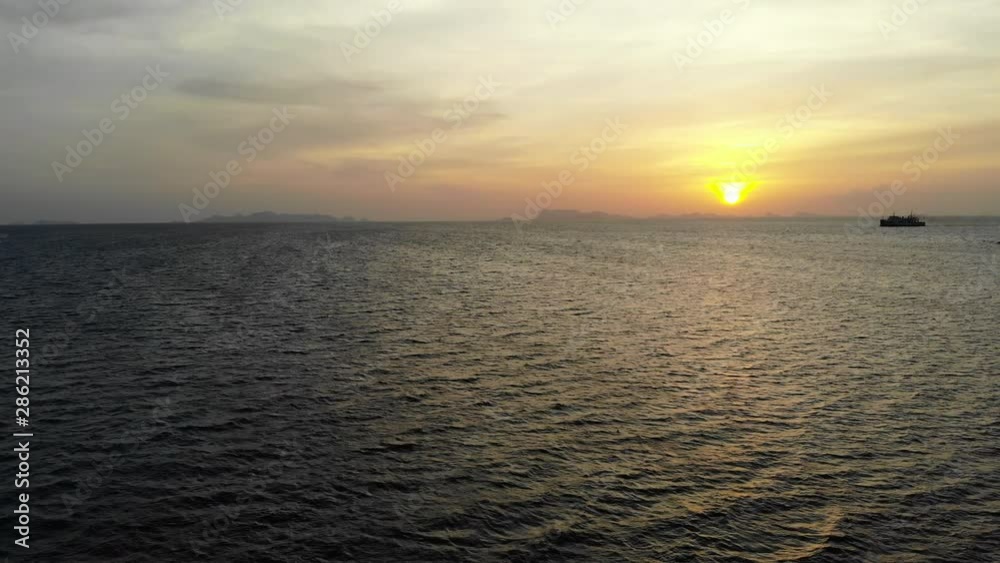 The sunsets over the waves spreading across the open ocean. A large ship slowing moves along the horizon.