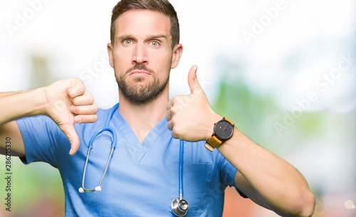 Handsome doctor man wearing medical uniform over isolated background Doing thumbs up and down, disagreement and agreement expression. Crazy conflict