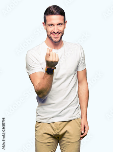 Handsome man wearing casual white t-shirt Beckoning come here gesture with hand inviting happy and smiling