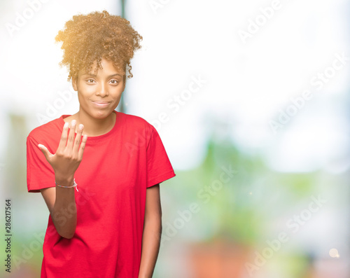 Beautiful young african american woman over isolated background Beckoning come here gesture with hand inviting happy and smiling © Krakenimages.com