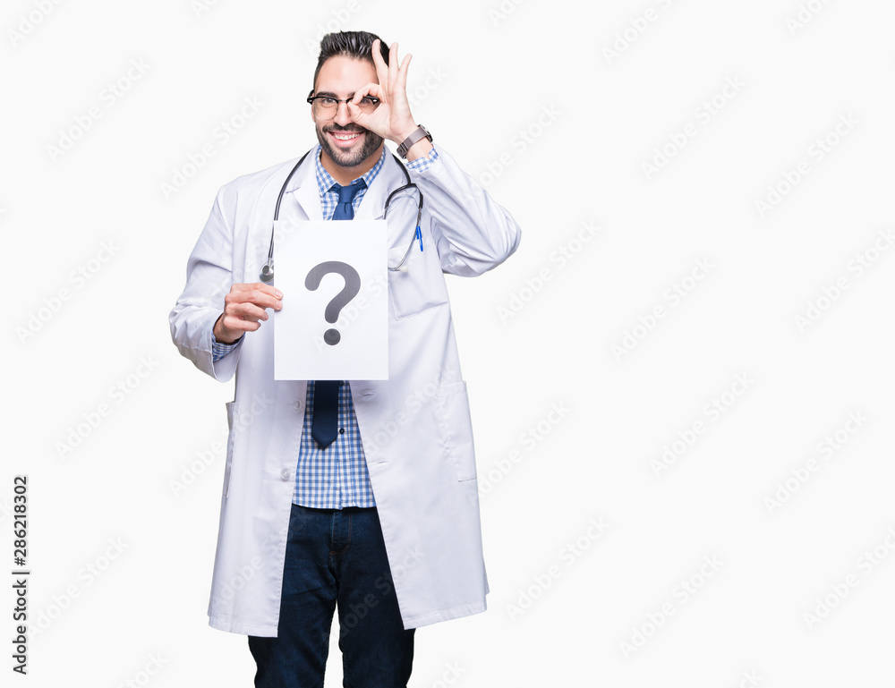 Handsome young doctor man holding paper with question mark over isolated background with happy face smiling doing ok sign with hand on eye looking through fingers Handsome young doctor man holding paper with question mark over isolated background with happy face smiling doing ok sign with hand on eye looking through fingers