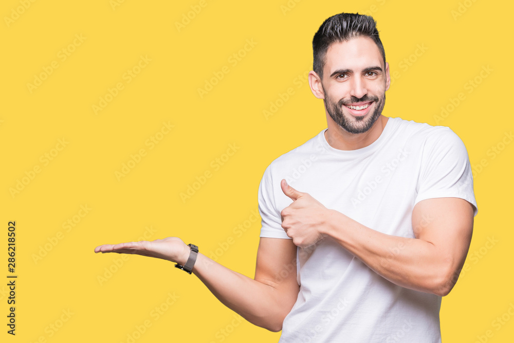 Handsome man wearing white t-shirt over yellow isolated background Showing palm hand and doing ok gesture with thumbs up, smiling happy and cheerful Handsome man wearing white t-shirt over yellow isolated background Showing palm hand and doing ok gesture with thumbs up, smiling happy and cheerful