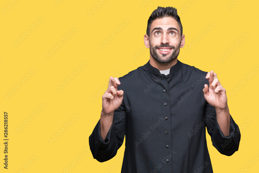 Young Christian priest over isolated background smiling crossing fingers with hope and eyes closed. Luck and superstitious concept. Young Christian priest over isolated background smiling crossing fingers with hope and eyes closed. Luck and superstitious concept.