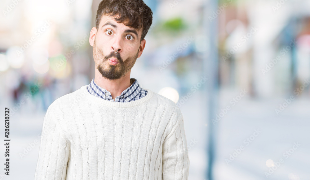 Young handsome man wearing winter sweater over isolated background making fish face with lips, crazy and comical gesture. Funny expression. Young handsome man wearing winter sweater over isolated background making fish face with lips, crazy and comical gesture. Funny expression.