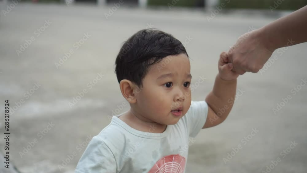 Child Asian boy learns to walk on the green grass in the park and holding hands mother. Child Asian boy learns to walk on the green grass in the park and holding hands mother.