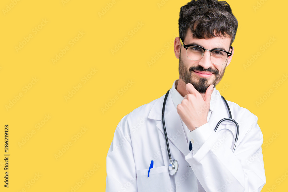 Young doctor man wearing hospital coat over isolated background looking confident at the camera with smile with crossed arms and hand raised on chin. Thinking positive. Young doctor man wearing hospital coat over isolated background looking confident at the camera with smile with crossed arms and hand raised on chin. Thinking positive.