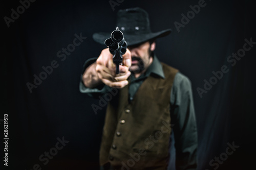 A cowboy aiming a revolver handgun at the viewer, dark studio background.