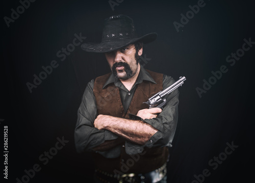 Cowboy standing with crossed arms  holding a revolver handgun.