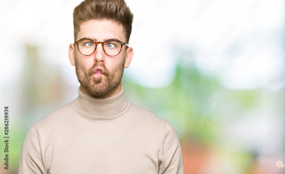 Obraz premium Young handsome business man wearing glasses making fish face with lips, crazy and comical gesture. Funny expression.