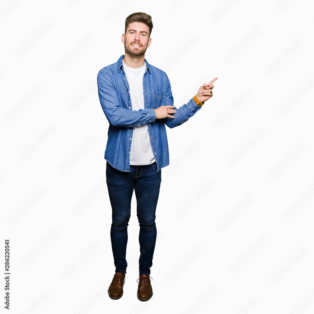 Young handsome blond man wearing casual denim jacket with a big smile on face, pointing with hand and finger to the side looking at the camera. Young handsome blond man wearing casual denim jacket with a big smile on face, pointing with hand and finger to the side looking at the camera.
