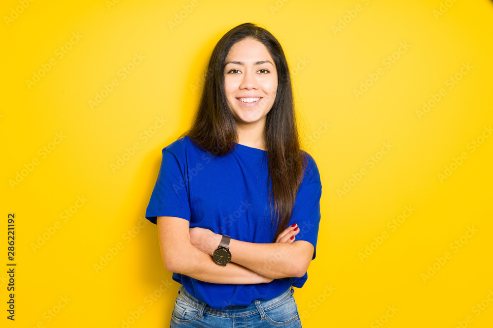 Beautiful young brunette woman standing with crossed arms and smiling over yellow isolated background Beautiful young brunette woman standing with crossed arms and smiling over yellow isolated background