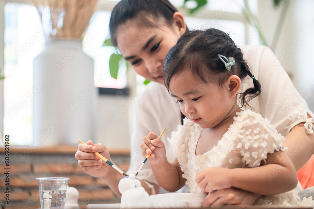 Asian pretty young mother and her daughter paining the plaster doll together. The mom looking the little girl  with happiness. Good relationship of mom and kid. Family activity and education concept.